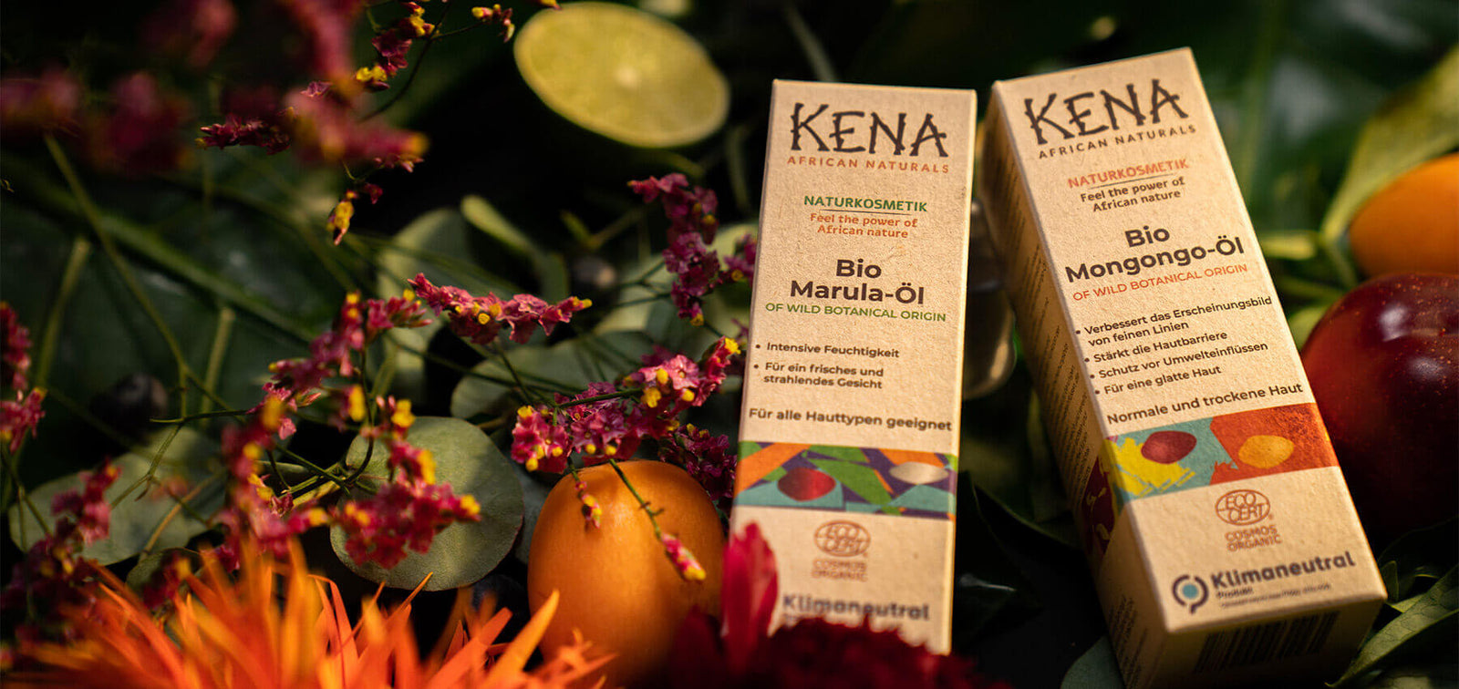KENA Bio Marula-Öl & Bio-Mongongo Öl Packungen liegen in der Natur umgeben von Früchten, Bättern und Blumen