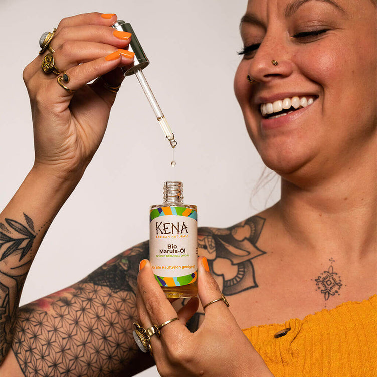 Bio Marulaöl von KENA African Naturals erfreute, lächelnde Frau tropft mit der Pipette einen Tropfen in die Glasflasche vom Produkt