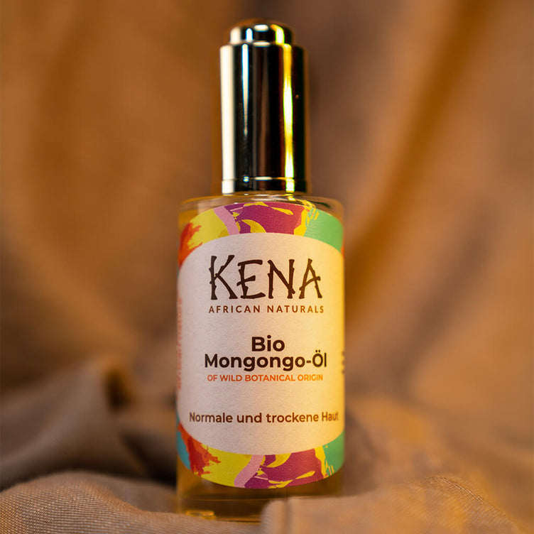 Bio Mongongo-Öl von KENA African Naturals Glasflasche in Nahaufnahme mit goldener Dropper Pipette mit Hintergund aus Stoff.