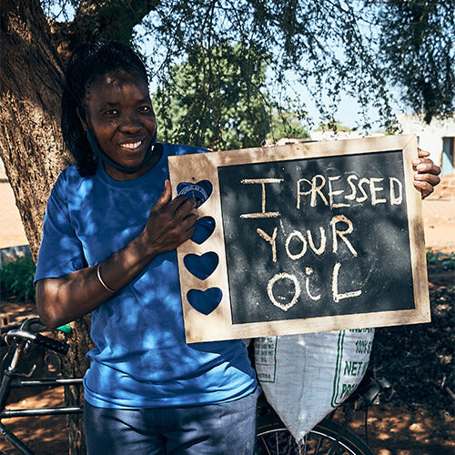 Afrikanische Arbeiterin in Botswana die ein Schild in den Händen hält „I pressed your oil“ Ich habe dein Öl gepresst