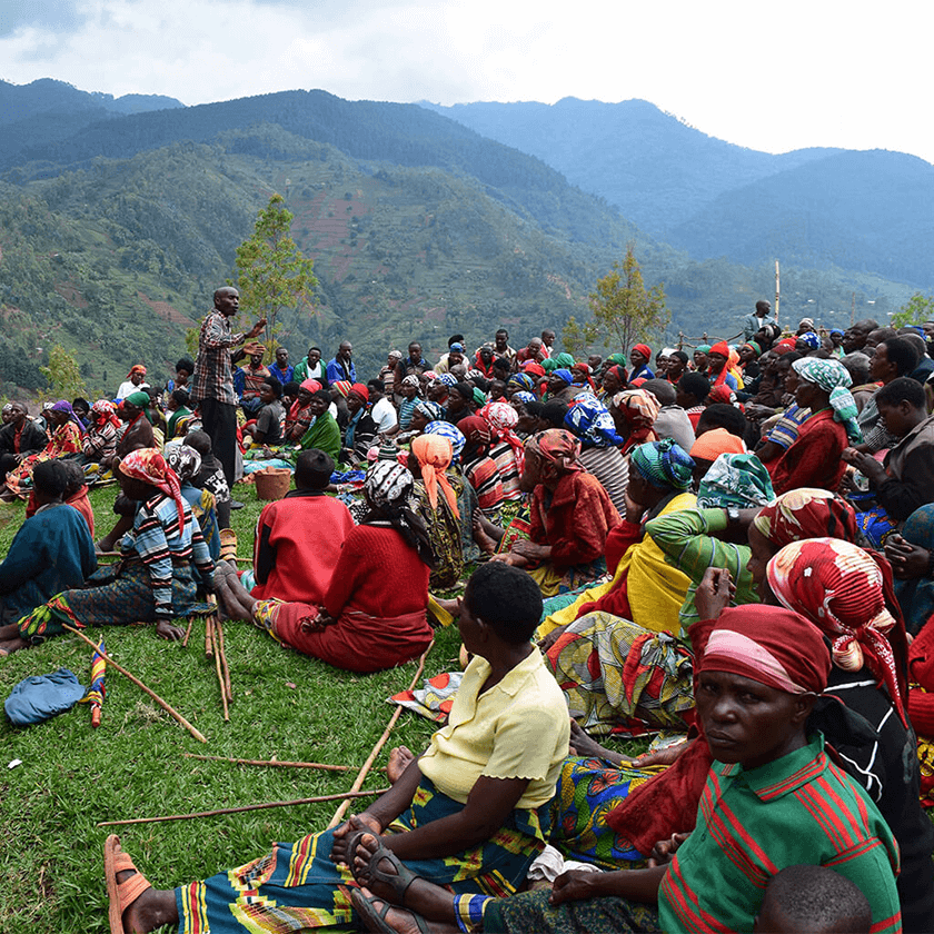 Versammlung von Frauen in Ruanda in der Natur, denen der neue Kochofen aus Lehm präsentiert wird.